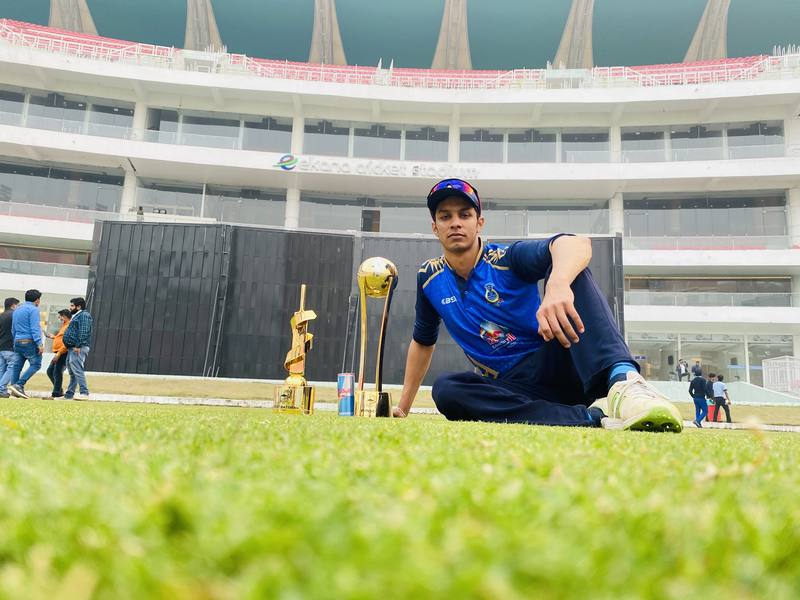 Rishab Saini seated on the outfield at Ekana Stadium with the trophies
