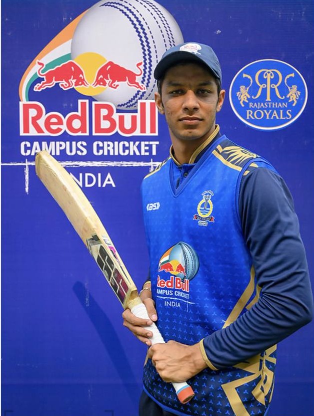 Rishab Saini holding a bat in front of the Red Bull Campus Cricket India backdrop